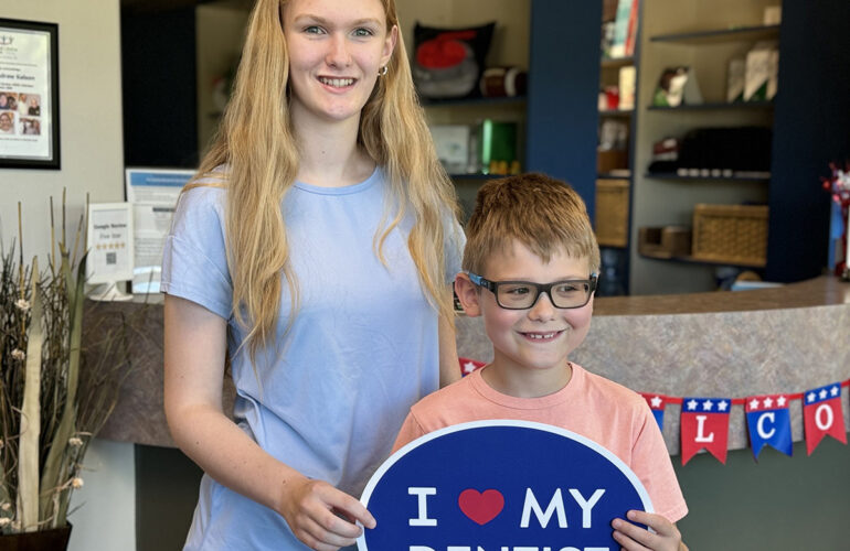 Woman and young boy smiling while holding a dental sign at a family dentistry office reception