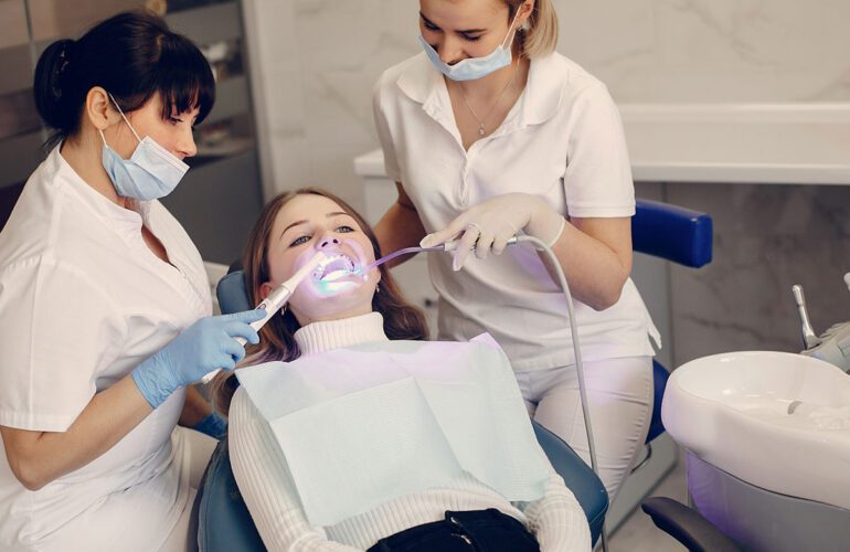 Two dental professionals performing a cosmetic dental treatment on a patient in a dental chair